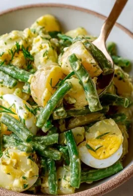 Creamy green bean potato salad in a bowl garnished with herbs.