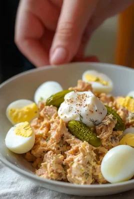 Bowl of tuna and egg salad garnished with fresh herbs and served on a plate.