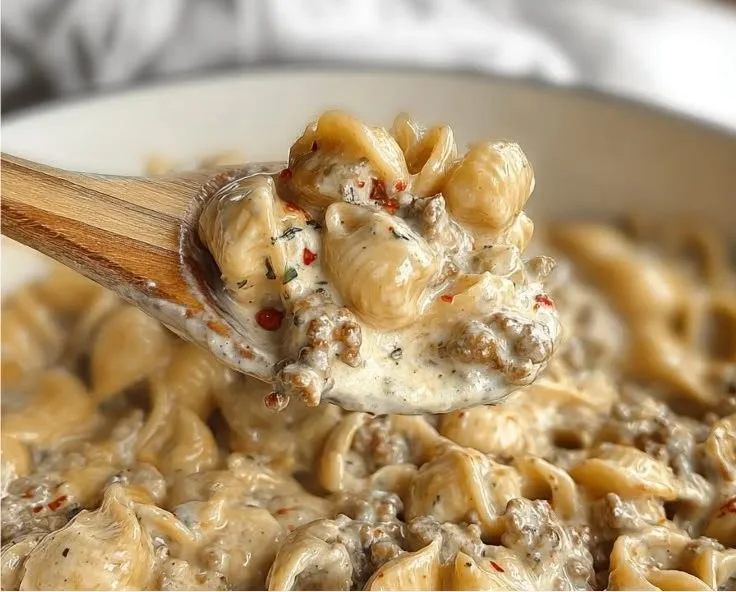 Bowl of creamy Italian sausage pasta garnished with herbs.