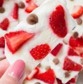 Frozen yogurt bark topped with strawberries and chocolate chips on a white plate