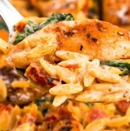 Creamy sun-dried tomato chicken orzo served in a bowl topped with herbs