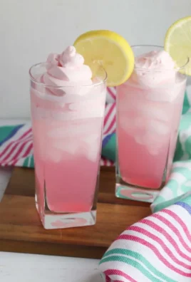 A refreshing glass of whipped pink lemonade topped with whipped cream and lemon slices.