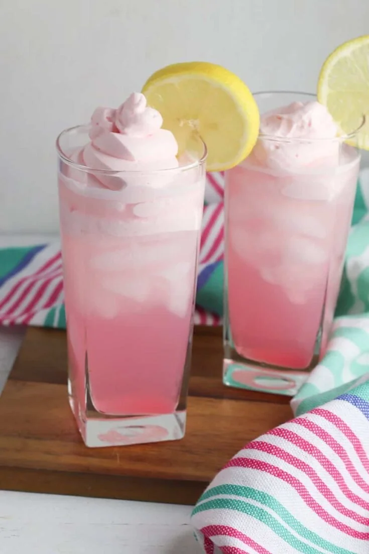 A refreshing glass of whipped pink lemonade topped with whipped cream and lemon slices.