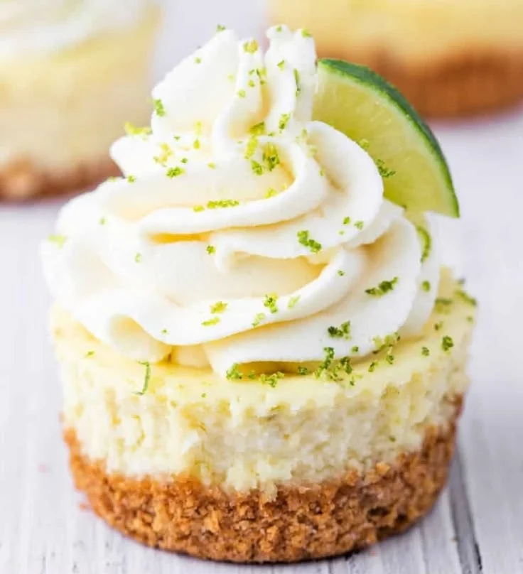Mini key lime cheesecakes topped with lime zest and whipped cream.