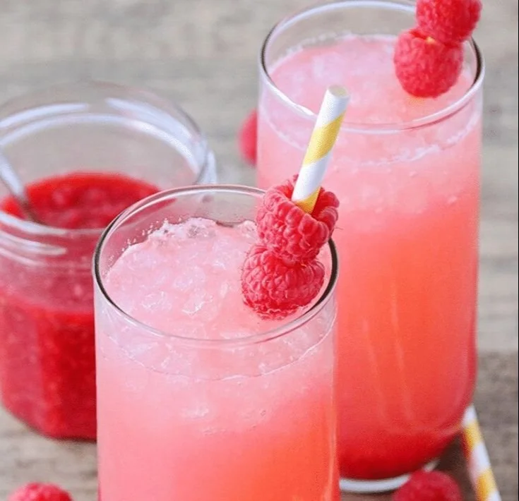 Glass of refreshing raspberry lemonade garnished with fresh raspberries and lemon slices.