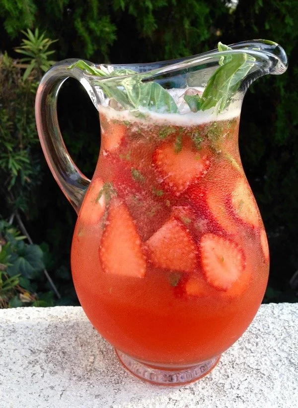 Glass of refreshing Strawberry Basil Lemonade with fresh strawberries and basil leaves.