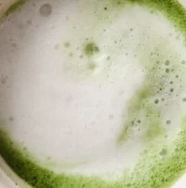 A creamy Vanilla Matcha Latte topped with frothy milk and vanilla essence.